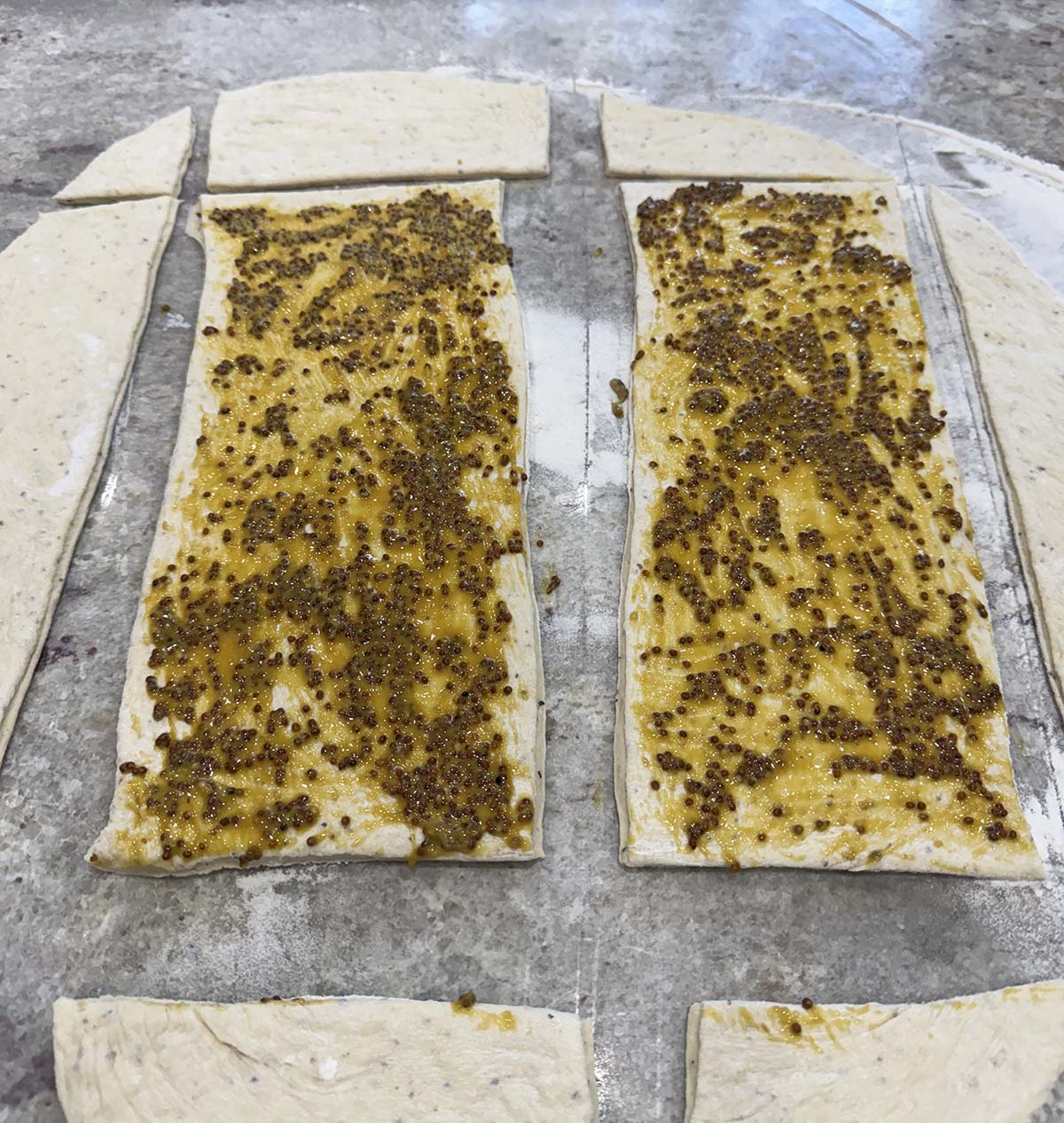 Herbed bread dough rolled out and topped with mustard spread.