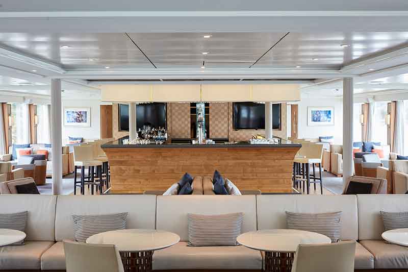 Observation bar abord ship is lined with floor to ceiling windows.